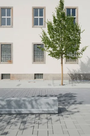 granite bench in front of a historic building and a small tree