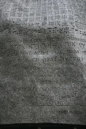 engraved text in multiple languages on a large dark boulder