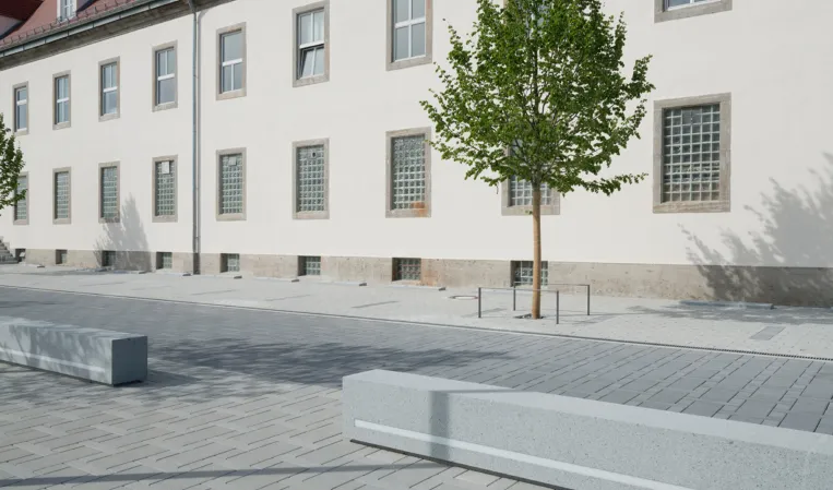 granite bench in front of a historic building and a small tree