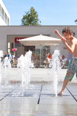 Wasserspiel mit interaktiven Fontänen auf dennen ein Kind spielt