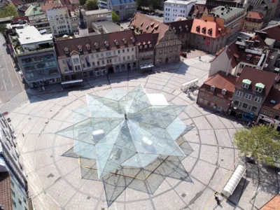 a large town square with a paving of granite and a star-shaped glass structure in the middle