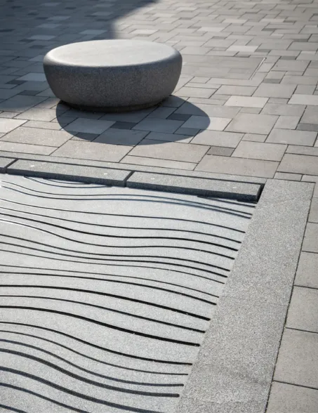 Bodengleiches Wasserfontänenfeld aus dunklem Granit mit eingraviertem Muster und Sitzpoller in der Nähe