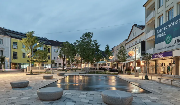 Fontänenfeld aus Granit mit Sitzpollern aus Stein bei Nacht
