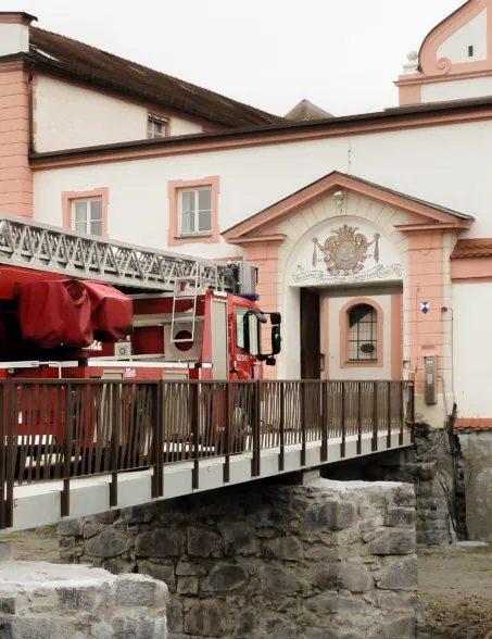 Ein Feuerwehrfahrzeug das über die Granitbrücke vor einem Schloss drüber fährt